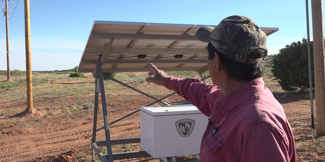 Ernest Littlefoot, Sr. shows the newly installed powerline poles near his home as part of the Light Up Navajo Project.