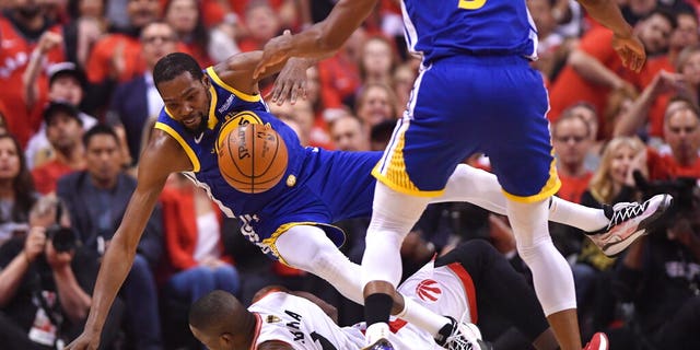 Golden State Warriors forward Kevin Durant, left, falls over Toronto Raptors center Serge Ibaka, bottom, as Warriors forward Andre Iguodala (9) looks on during first-half basketball game action in Game 5.