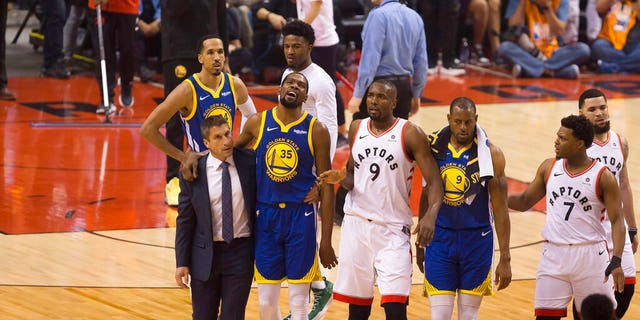 Golden State Warriors forward Kevin Durant (35) walks off the court after sustaining an injury as he is consoled by Toronto Raptors center Serge Ibaka (9) as Warriors forward Andre Iguodala (9) and guard Kyle Lowry (7) look on during first-half basketball action in Game 5 of the NBA Finals in Toronto, Monday, June 10, 2019. (Chris Young/The Canadian Press via AP)