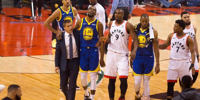 Golden State Warriors forward Kevin Durant (35) walks off the court after sustaining an injury as he is consoled by Toronto Raptors center Serge Ibaka (9) as Warriors forward Andre Iguodala (9) and guard Kyle Lowry (7) look on during first-half basketball action in Game 5 of the NBA Finals in Toronto, Monday, June 10, 2019. (Chris Young/The Canadian Press via AP)