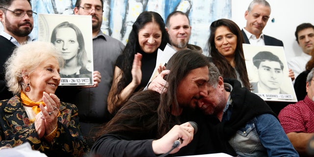 Javier Matías Darroux Mijalchuk, center, is greeted by his biological uncle Roberto Mijalchuk, right, as Estela de Carlotto, left, president of The Grandmothers of Plaza de Mayo, and others applaud during a news conference in Buenos Aires, Argentina.