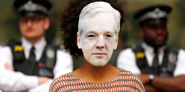 Police watch an Assange supporter wearing a mask and protesting at Westminster Magistrates Court in London, Friday, June 14, 2019. WikiLeaks founder Julian Assange is expected to appear at hearing in a London court via video link as he continues his fight against extradition to the United States.