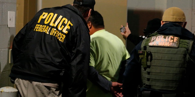 In this Oct. 22, 2018, file photo, U.S. Immigration and Customs Enforcement agents escort a target to lockup during a raid in Richmond, Va. Carrying out President Donald Trump's hard-line immigration policies has exposed ICE to unprecedented public scrutiny and criticism. (AP Photo/Steve Helber, File)