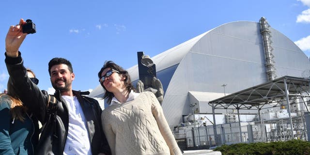 Tourists in the Exclusion Zone take selfies in front of the New Safe Confinement Structure, completed in 2017, which covers the fourth reactor of the Chernobyl nuclear power plant.