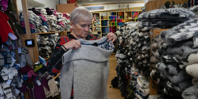 In this photo taken on Tuesday, April 30, 2019, Thuridur Einarsdottir, founder of the Handknitting Association of Iceland, folds a 'lopi' sweater in Reykjavik. Trouble is rattling one of Iceland’s most distinctive industries: the production of the thick, hand-knitted “lopi” sweaters adored by tourists and worn with pride by locals. The individually produced, very warm sweaters have become a symbol of Iceland. But increasingly the local wool is being shipped to the cheaper labor market of China, where the sweaters are hand-knitted and then sent back for sale on the North Atlantic island. (AP Photo/Egill Bjarnason)