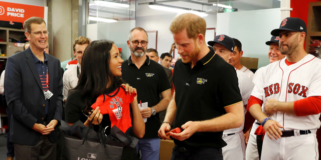 Duchess Meghan (L) and Prince Harry (R) are gifted a onesie from the Boston Red Sox. 