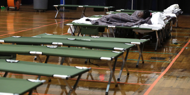 In this June 13, 2019 photo, a migrant woman sleeps on a cot inside the Portland Exposition Building in Portland, Maine. Maine's largest city has repurposed the basketball arena as an emergency shelter in anticipation of hundreds of asylum seekers who are headed to the state from the U.S. southern border. Most are arriving from Congo and Angola. (AP Photo/Elise Amendola)