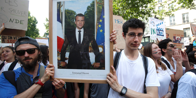 FILE - In this photo taken on Friday May 24, 2019, youths hold the official portrait of French President Emmanuel Macron during a climate march in Paris.Six French activists were convicted Wednesday June 12, 2019 for theft after taking down an official portrait of President Emmanuel Macron to protest his climate change policies they consider as not strong enough. (AP Photo/Michel Euler, File)