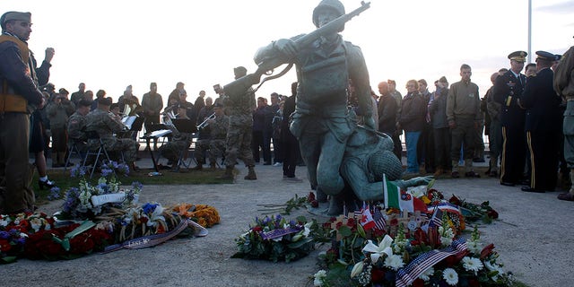 floral tributes are placed at the National Guard Monument Memorial as members of the USAREUR band play in the background near Omaha Beach, in Normandy, France, on Thursday. (Associated Press)