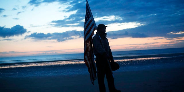 Udo Hartung from Frankfurt, Germany, a World War II reenactor, holds the U.S. flag as he stands at dawn on Omaha Beach, in Normandy, France on Thursday. (Associated Press)
