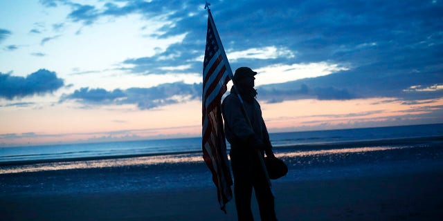 Udo Hartung from Frankfurt, Germany, a World War II reenactor, holds the U.S. flag as he stands at dawn on Omaha Beach, in Normandy, France on Thursday. (Associated Press)