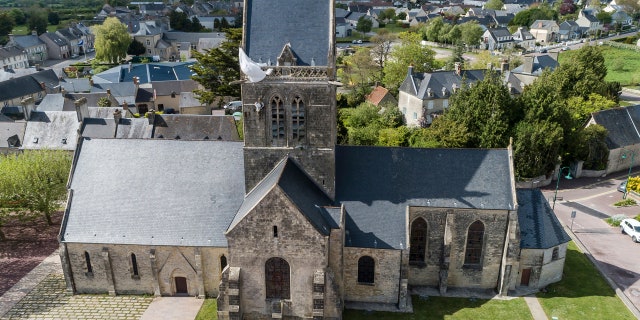 In this photo taken with a drone, a dummy paratrooper representing a WWII paratrooper from the 82nd Airborne hangs on the bell tower of the church of Sainte Mere Eglise, in Normandy, France, Thursday, May 9, 2019. Seventy-five years ago, American paratrooper John Steele dangled from a clock tower in Sainte-Mere-Eglise after his parachute got caught during the D-Day invasion, and survived. (AP Photo/David Vincent)