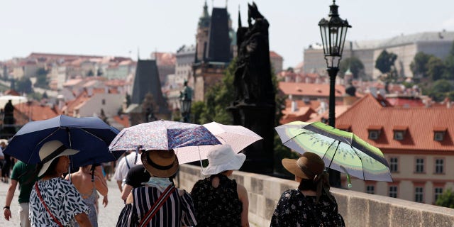 Tourists use umbrellas to shield themselves from the sun as they cross the medieval Charles Bridge on a hot day in Prague, Czech Republic, Wednesday, June 26, 2019.