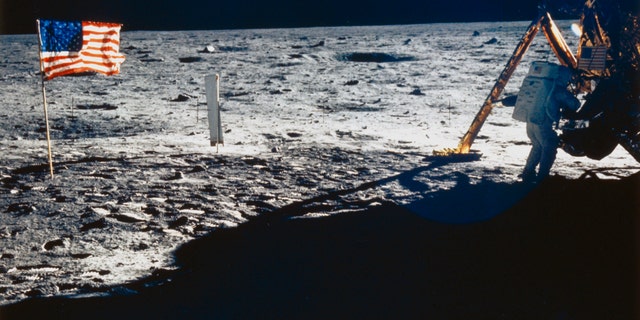 Neil Armstrong is shown beside the Lunar Module. Also visible are the U.S. flag and the solar wind experiment which was flown on all the Apollo missions.
