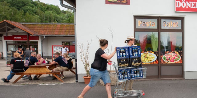 A woman and a man push a shopping cart with beer crates along the street near a local supermarket to protest the Shield and Sword Festival. (Photo by Daniel Schäfer/picture alliance via Getty Images)
