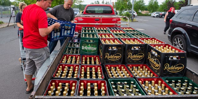 A woman and two men load beer crates near a local supermarket onto a trailer. (Photo by Daniel Schäfer/picture alliance via Getty Images)