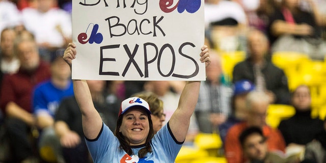 FILE - In this April 3, 2015, file photo, a fan holds up a sign during a pregame ceremony as the Toronto Blue Jays face the Cincinnati Reds in an exhibition baseball game in Montreal. The Tampa Bay Rays have received permission from Major League Baseball's executive council to explore a plan that could see the team split its home games between the Tampa Bay area and Montreal. (Paul Chiasson/The Canadian Press via AP, File)