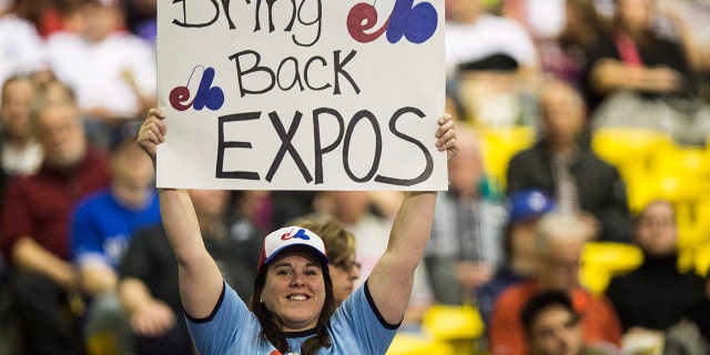 FILE - In this April 3, 2015, file photo, a fan holds up a sign during a pregame ceremony as the Toronto Blue Jays face the Cincinnati Reds in an exhibition baseball game in Montreal. The Tampa Bay Rays have received permission from Major League Baseball's executive council to explore a plan that could see the team split its home games between the Tampa Bay area and Montreal. (Paul Chiasson/The Canadian Press via AP, File)