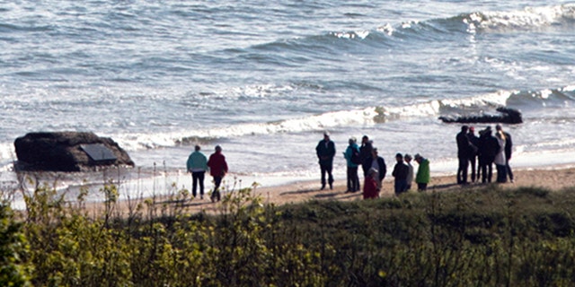 People stand near a memorial plaque for World War II medics on Omaha Beach at the foot of Normandy American Cemetery in Colleville-sur-Mer, France, Friday, May 3, 2019. (AP Photo/Virginia Mayo)