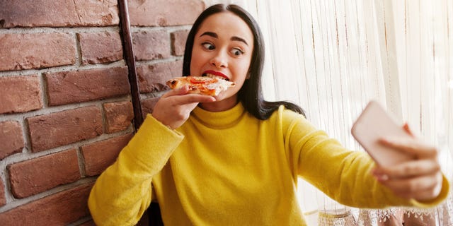 A young woman takes a selfie while biting into a slice of pizza. Cell phones have become a "personal extension" of our lives, said one psychologist.