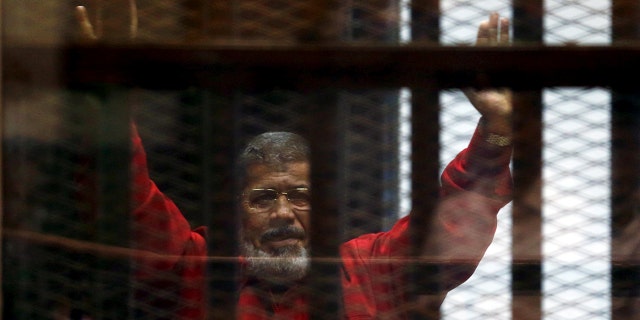 In this 2015 photo, Egypt's deposed president Mohamed Mursi greets his lawyers and people from behind bars at a court hearing.