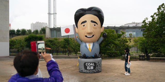 A large inflatable depicting Japanese Prime Minister Shinzo Abe stands in front of a coal-fired power plant during a priests held to demand an to coal funding ahead of the G20 Summit Thursday, June 27, 2019, in Kobe, Japan. (AP Photo/Jae C. Hong)