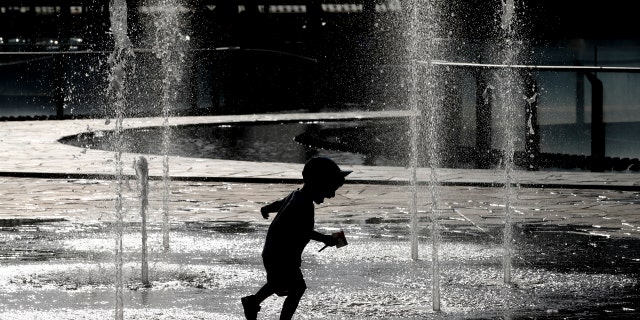 A children plays and cool-off as water sprinkles from a fountain, in Milan, Italy, Monday, June 24, 2019.