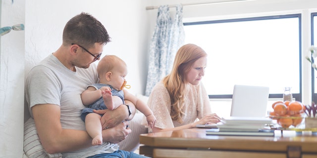 Dad hugs his daughter at the kitchen table, and mom checks the email next to him, excluding the baby.