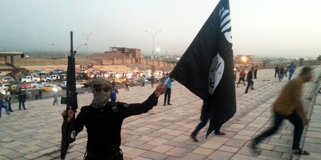 An ISIS fighter holds a flag and a weapon on a street in the city of Mosul in 2014.