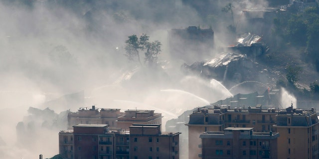 Fire hoses spray water to reduce dust triggered by the planned blast which demolished the remaining spans of the Morandi bridge, in Genoa, Italy, Friday, June 28, 2019. (AP Photo/Antonio Calanni)