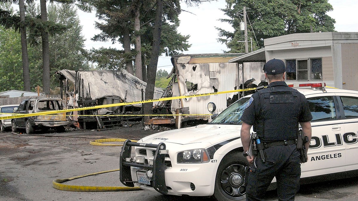 Port Angeles police Officer T.J. Mueller looks over the scene of a fire that destroyed two mobile homes and left several dead early Saturday, July 6, 2019.  (Associated Press)