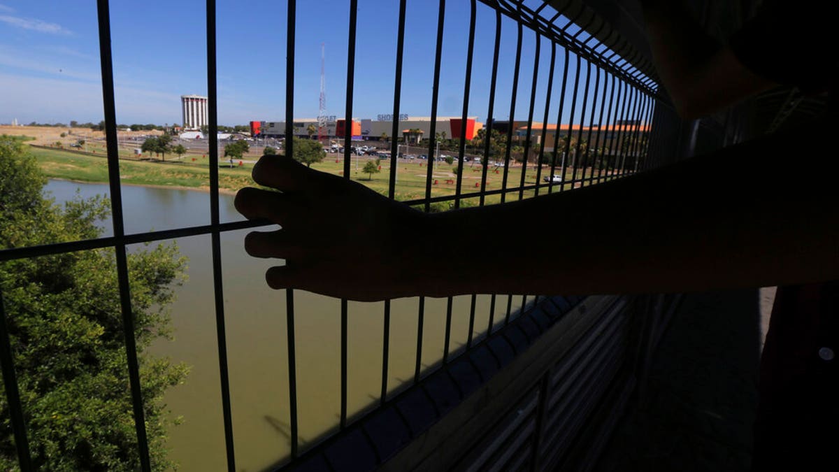 The hand of a youth from Nuevo Laredo rests on the gate as he stops to watch a train pass, above the Rio Grande river on International Bridge 1 Las Americas, a legal port of entry which connects Laredo, Texas in the U.S. with Nuevo Laredo, Mexico, Thursday, July 18, 2019.