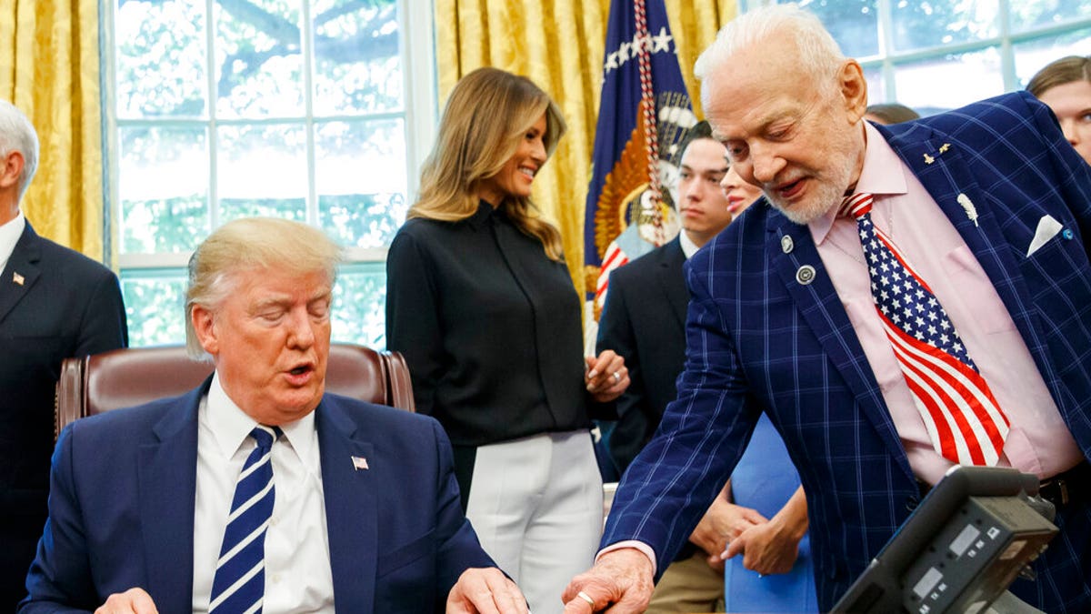 President Donald Trump receives a gift from Apollo 11 astronaut Buzz Aldrin, with first lady Melania Trump, during a photo opportunity commemorating the 50th anniversary of the Apollo 11 moon landing in the Oval Office of the White House, Friday, July 19, 2019, in Washington.