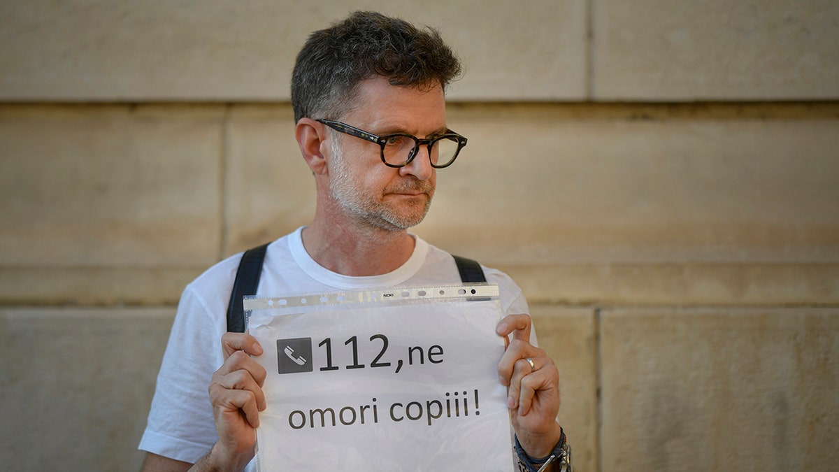 A man holding a paper displaying the country's emergency number that reads "112, you are killing our children" outside the Interior Ministry, in Bucharest, Romania, on Friday. (AP Photo/Andreea Alexandru)