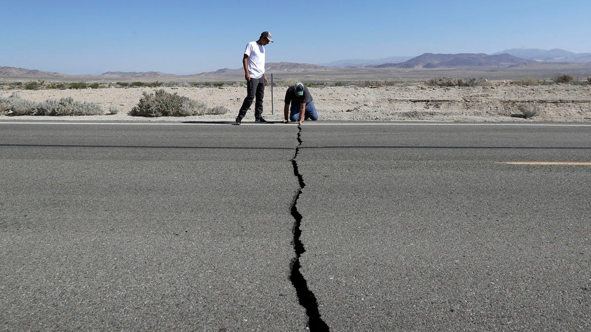 Ron Mikulaco, right, and his nephew, Brad Fernandez, examine a crack caused by an earthquake on Highway 178, Saturday, July 6, 2019, outside of Ridgecrest, Calif.