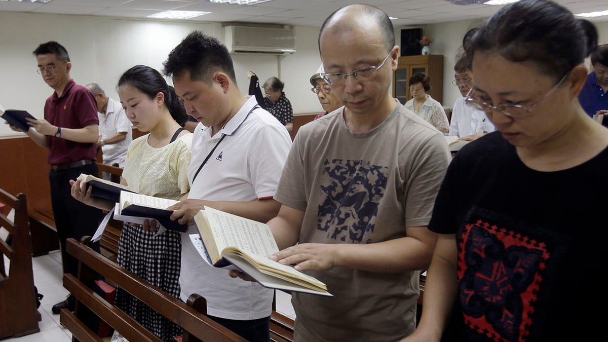 In this Sunday, July 7, 2019, photo, from right; Ren Dejun, Liao Qiang, Peng Ran and Ren Ruiting follow a hymn book during service at a church in Taipei, Taiwan. The Sunday service this week at an unassuming church in Taiwan was especially moving for one man, Liao Qiang. It was the first time he had worshipped publicly since authorities shut down his church in China seven months ago. (AP Photo/Chiang Ying-ying)