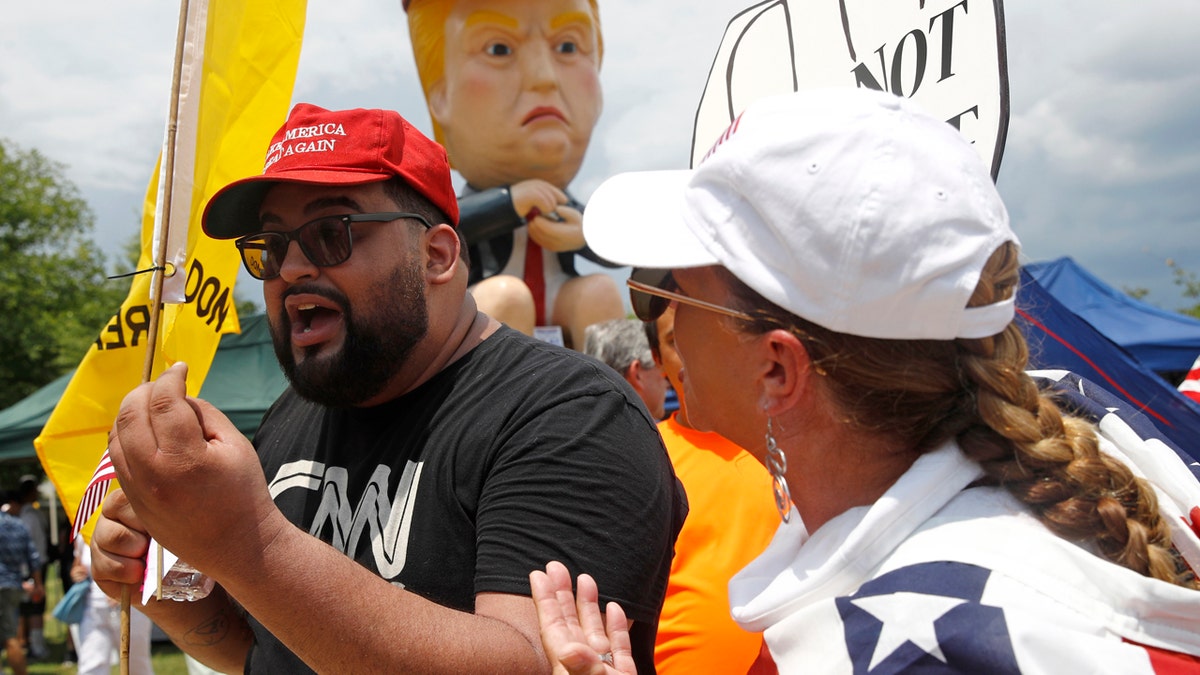 A supporter of President Donald Trump who gave his name as Moto Moto, left, of Brooklyn, N.Y., debates with protesters in front of a sculpture of President Trump holding a cell phone while sitting on a toilet before Independence Day celebrations, Thursday, July 4, 2019, on the National Mall in Washington. (AP Photo/Patrick Semansky)
