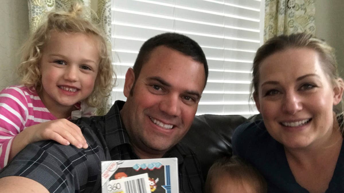 In this June 15, 2019 photo provided by Heritage Auctions, Scott Amos, along with his wife, Kristy, and daughters Grace, left, and Katie, pose in Reno, Nev., with an unopened copy of a 1987 cult-classic video game "Kid Icarus."