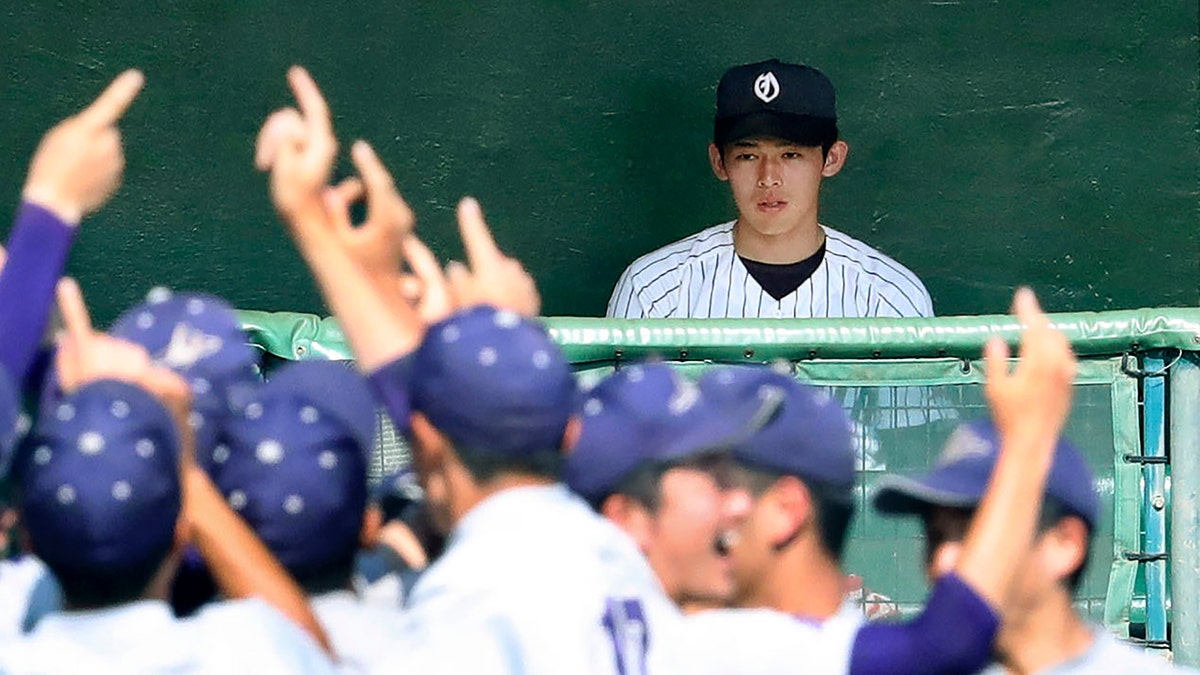 In this July 25, 2019, photo, Ofunato High School pitcher Roki Sasaki on the bench watches Hanamaki Higashi High School players celebrate their 12-2 win in their final baseball game at the Iwate Prefecture qualifier in Morioka, northern Japan. (Kyodo News via AP)