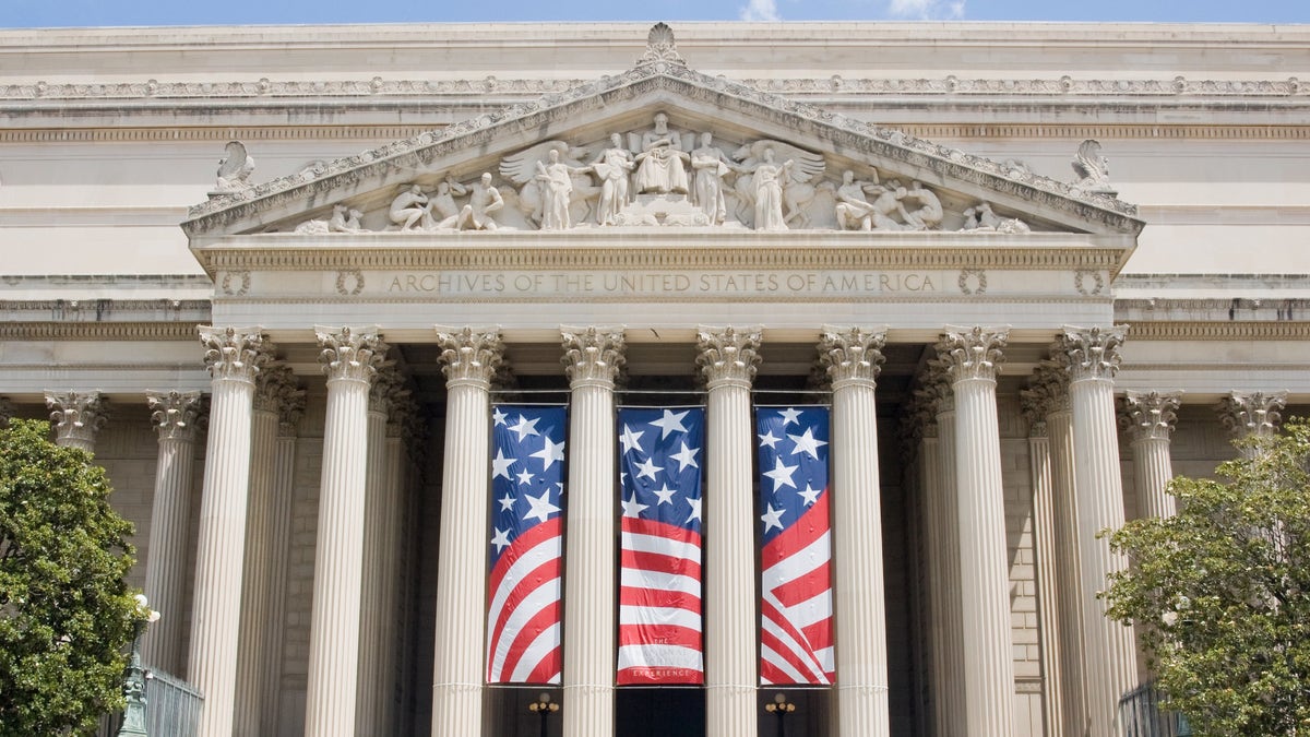United States National Archives in Washington, DC with a huge flag hanging on its columns.