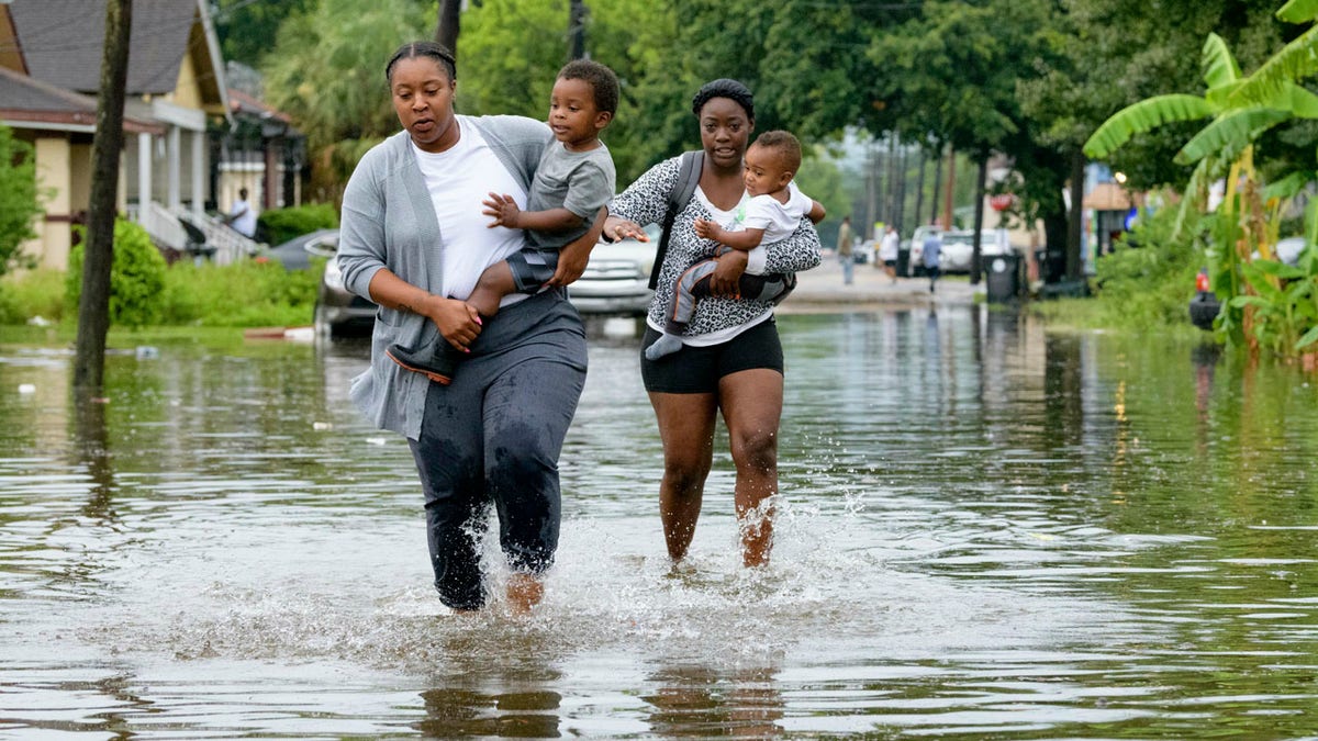 Jalana Furlough carries her son Drew Furlough as Terrian Jones carries Chance Furlough on Belfast Street near Eagle Street in New Orleans after flooding from a tropical wave system in the Gulf Mexico that dumped lots of rain in Wednesday, July 10, 2019.