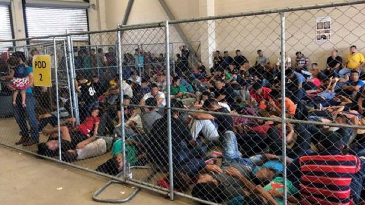 Detainees at a McAllen, Texas Border Patrol facility are observed by government inspectors crowded behind a fence. 