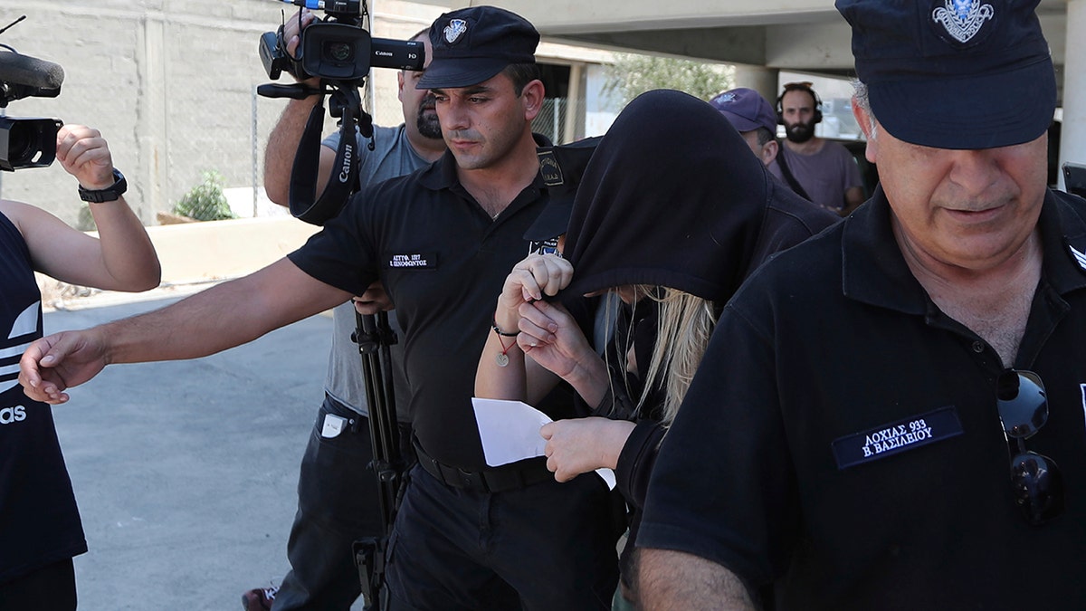 Elite police unit officers escort a 19-year old British woman, center with head covered, to Famagusta court in Paralimni, Cyprus. (AP Photo/Petros Karadjias)