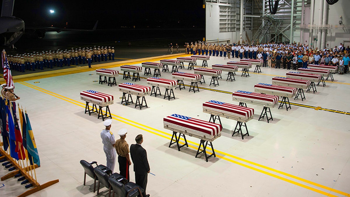 Service members and guests stand as "Taps" is played over transfer cases carrying the remains of unidentified service members lost in the Battle of Tarawa during World War II.