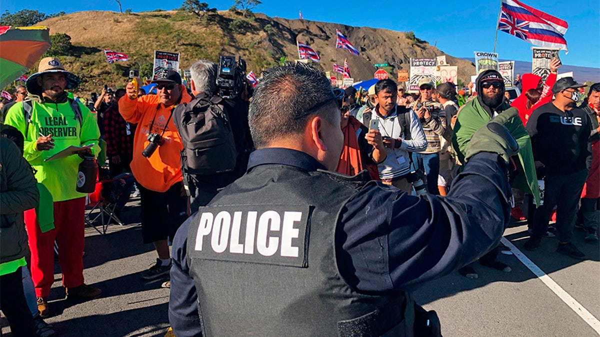 A police officer gestures at demonstrators blocking a road at the base of Hawaii's tallest mountain, on Monday, in Mauna Kea, Hawaii, who are protesting the construction of a giant telescope on land that some Native Hawaiians consider sacred. (AP)