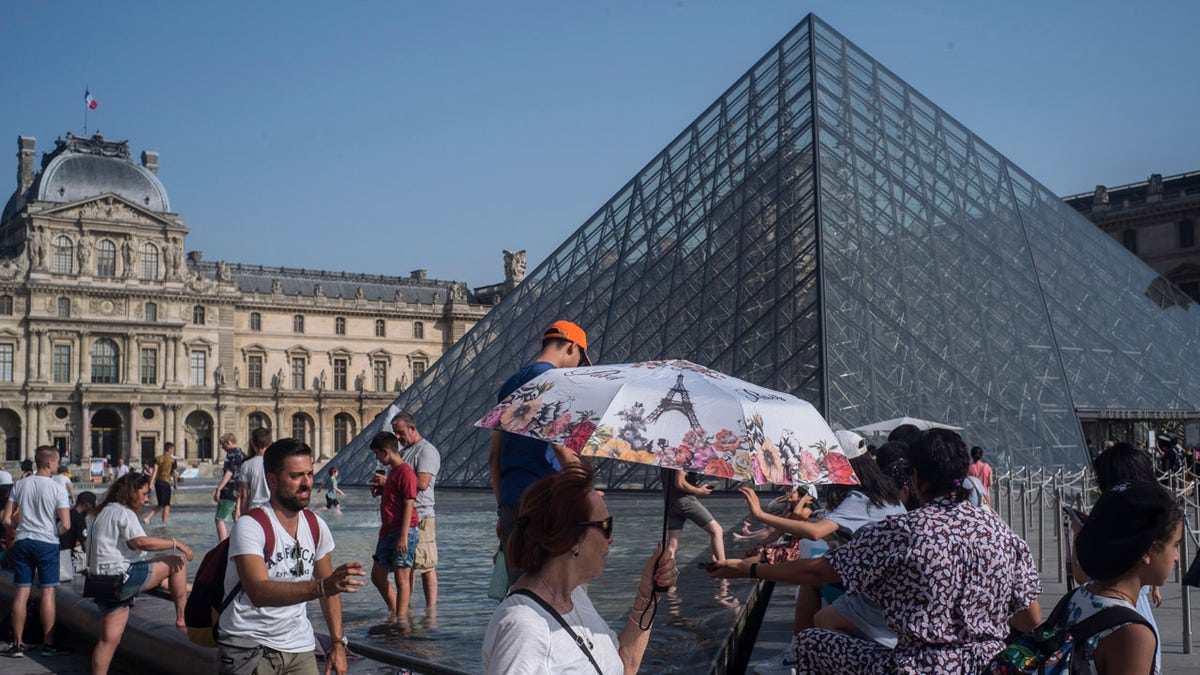 People cool off next to the fountains at Louvre Museum in Paris, France.