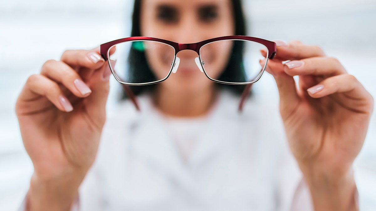 Cropped image of attractive young female doctor in ophthalmology clinic. Doctor ophthalmologist is standing near shelves with different eyeglasses.