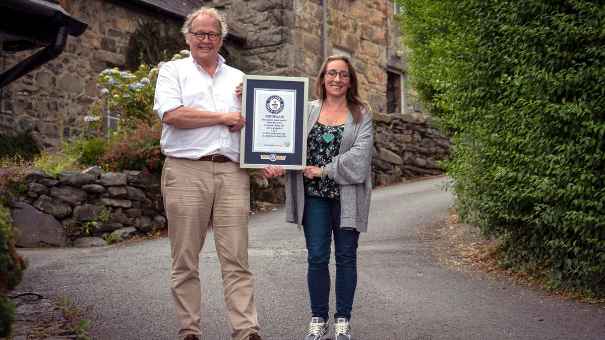 In this undated handout photo provided by Guinness World Records on Tuesday, July 16, 2019, Gwyn Headley and Sarah Badhan, stand on Ffordd Pen Llech with a certificate from Guinness World Records, confirming that the road is the steepest street in the world, in the seaside town of Harlech, North Wales.