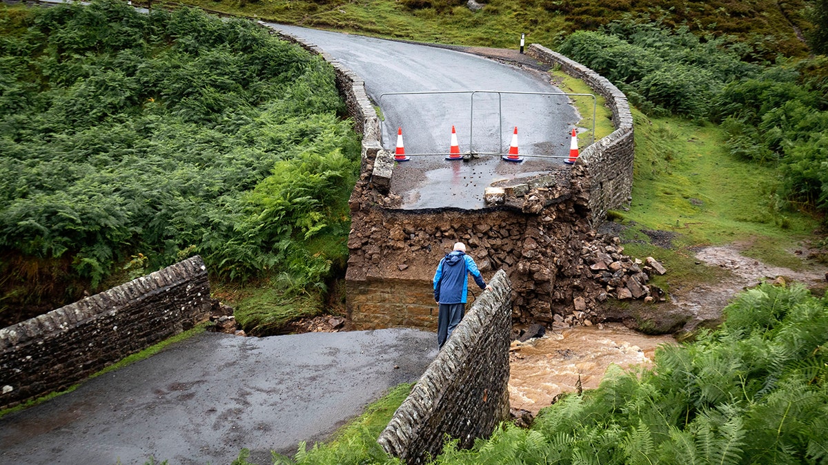 A man looks from the edge of a collapsed road bridge near Grinton, North Yorkshire, after parts of the region were inundated by overnight rain. (Danny Lawson/PA via AP)