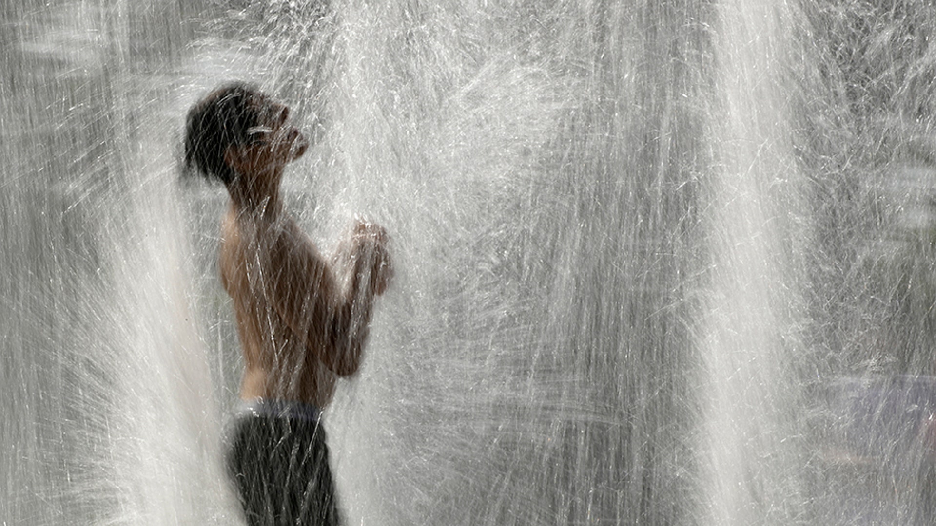 A boy plays in a fountain to cool off as temperatures approach 100 degrees Fahrenheit in Kansas City, July 18, 2019. 